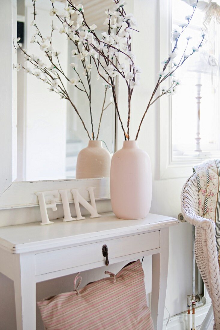 Vase mit Zweigen und Deko-Buchstaben auf weißem Wandtisch vor gerahmtem Spiegel