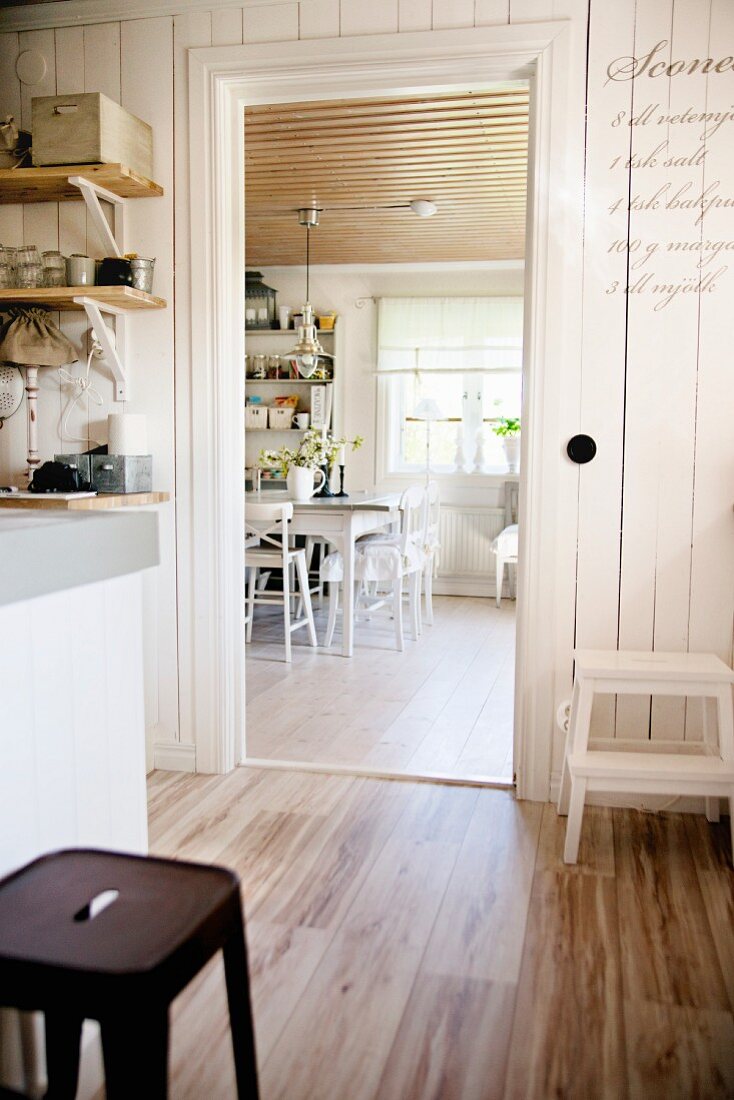 Ländliche Küche und teilweise sichtbarer Retro Hocker auf Dielenboden, im Hintergrund offene Tür und Blick ins Esszimmer