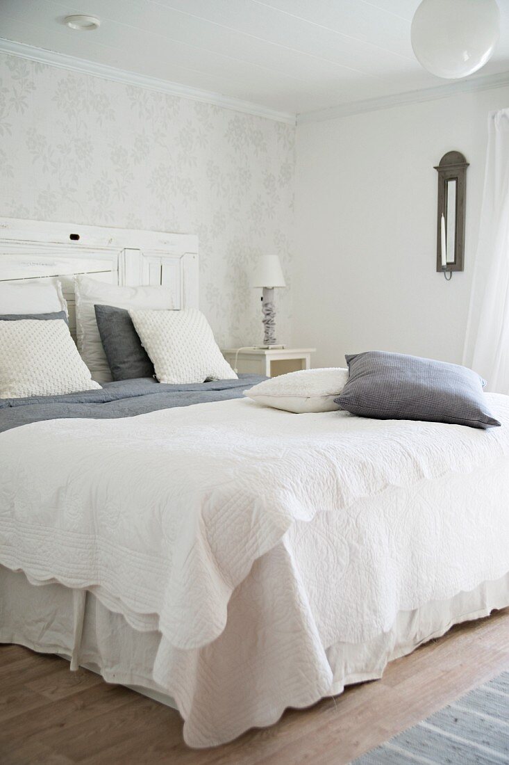 Doppelbett mit weisser Tagesdecke und Kissen in grauen und weissen Farbtönen in schlichtem Schlafzimmer