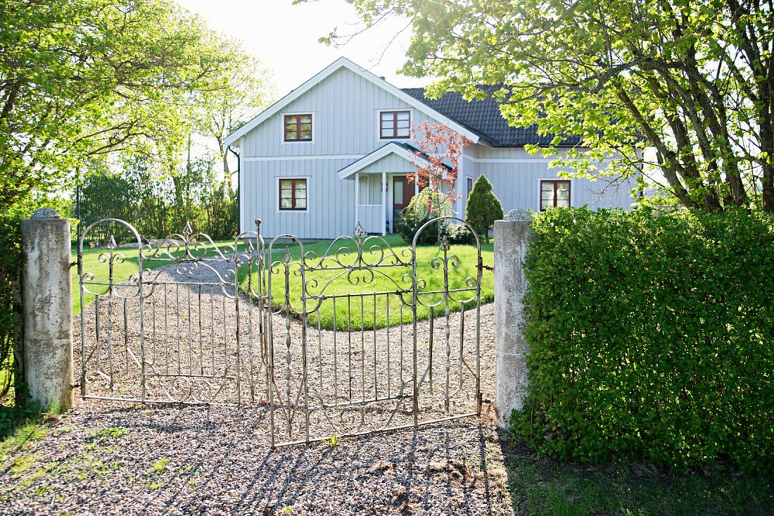 Wrought iron gate leading to garden and pale grey, clapboard country house