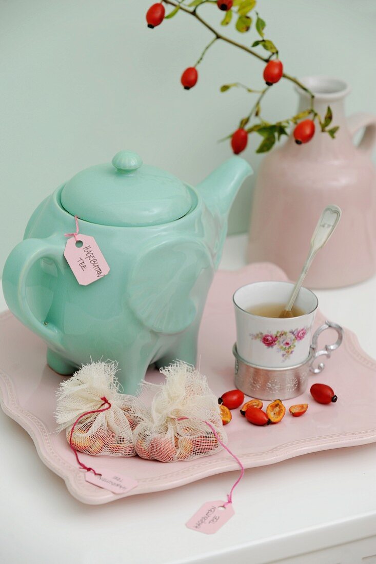 Turquoise teapot, vintage cup, halved rose hips and fabric teabags on pink serving tray