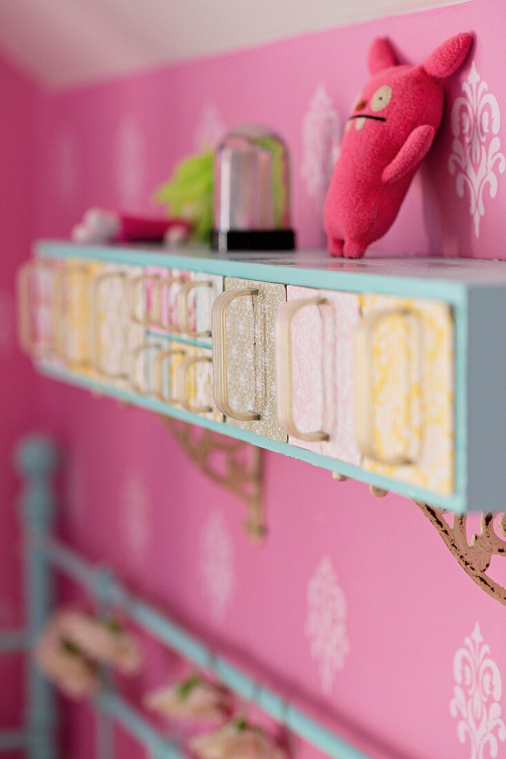 Cabinet with retro glass scoops mounted on wall with pink wallpaper