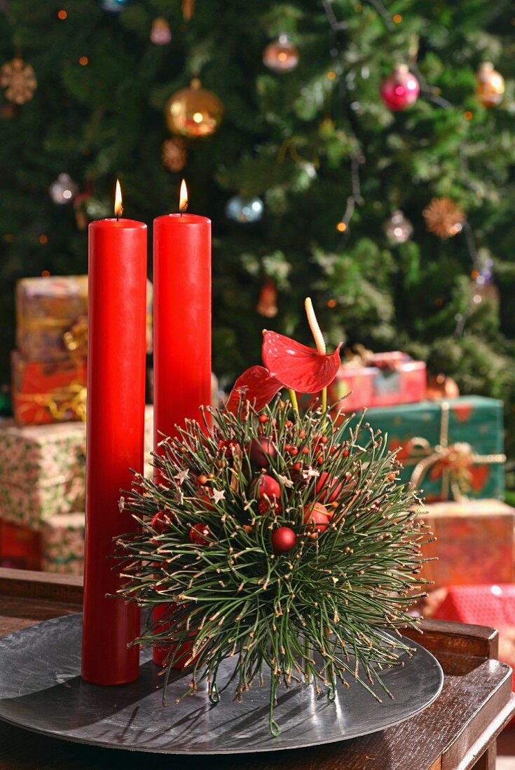 Hand-crafted, floating, spherical arrangement of fir twigs and red candles on metal dish in front of decorated Christmas tree