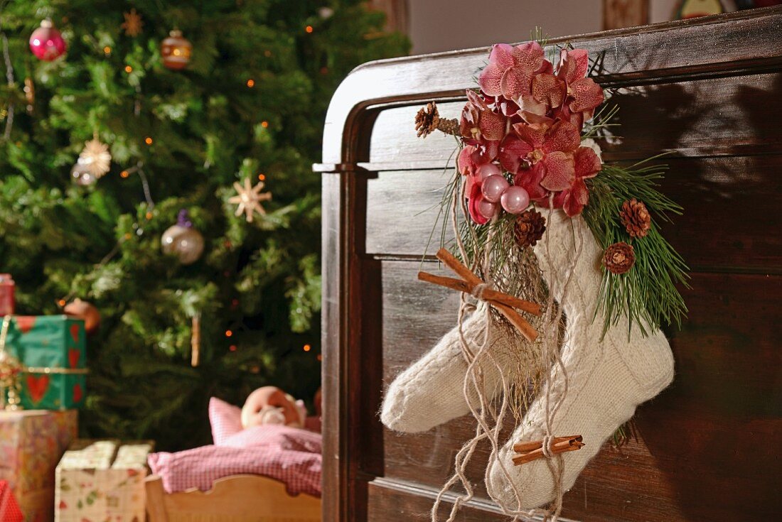 Wollsocken mit Orchideenblüten und Zimtstangen als Weihnachtsdekoration an Holzbettgestell, im Hintergrund Weihnachtsbaum