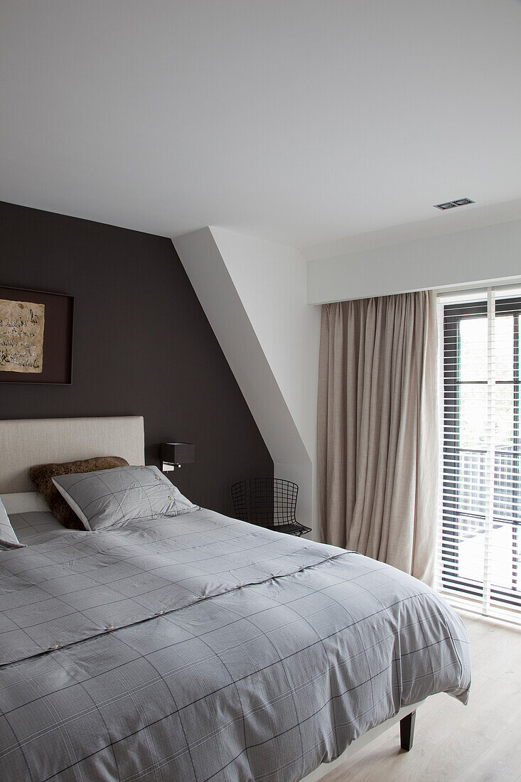Schlafzimmer mit schräger Wand, grauer Bettwäsche und bodenlangen Vorhängen