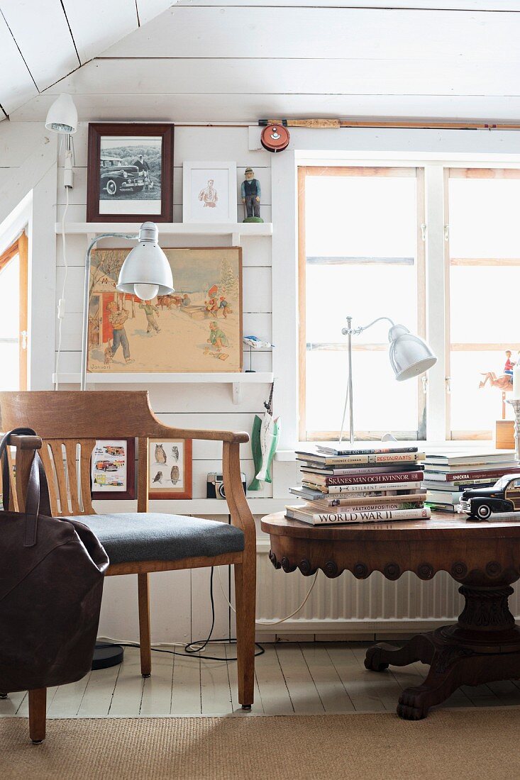Antiker Holztisch mit Büchern in weißem, holzverkleidetem Zimmer mit ländlichem Charme