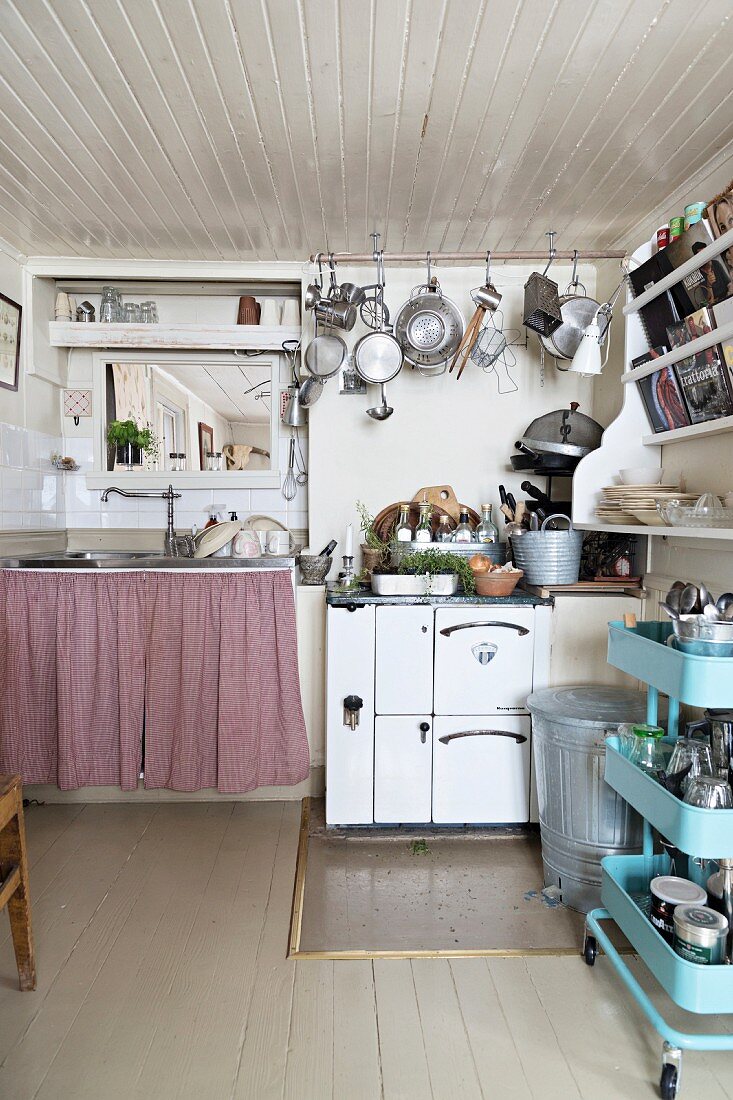 Retro, pale blue tea trolley, cooker and pots and pans hanging from rod in rustic kitchen