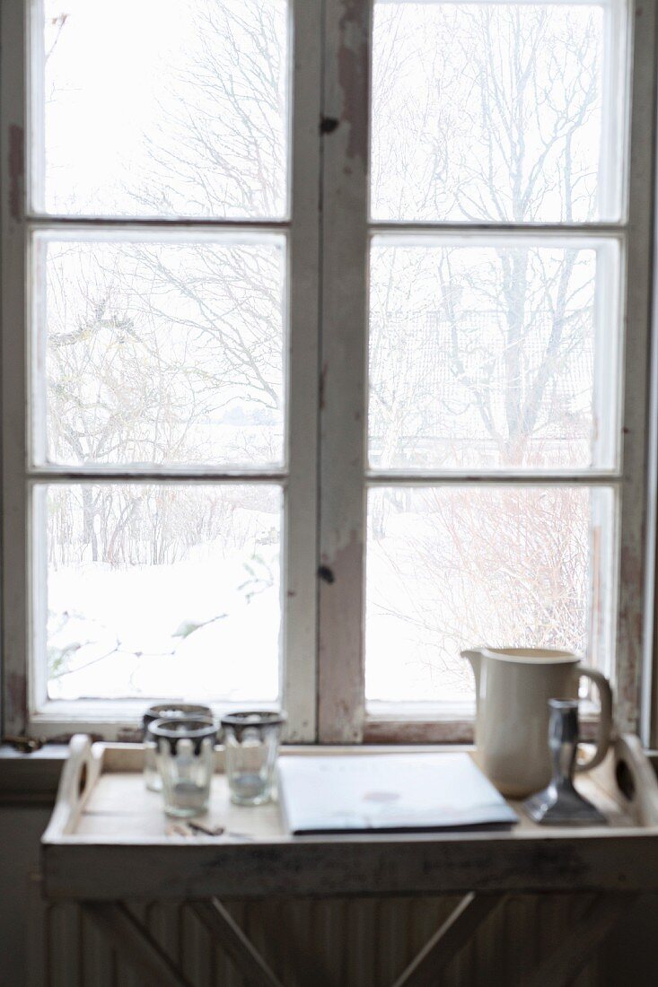 Tabletttisch mit Krug und Gläsern vor Fenster, Blick in verschneiten Garten