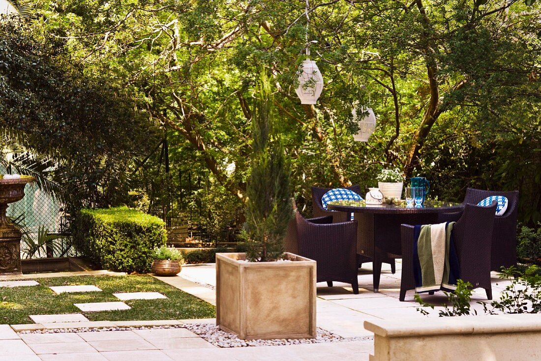 Gartenmöblierung und Pflanzenbehälter mit Zypresse auf gepflasterter Fläche in sonnigem Garten einer alten Villa
