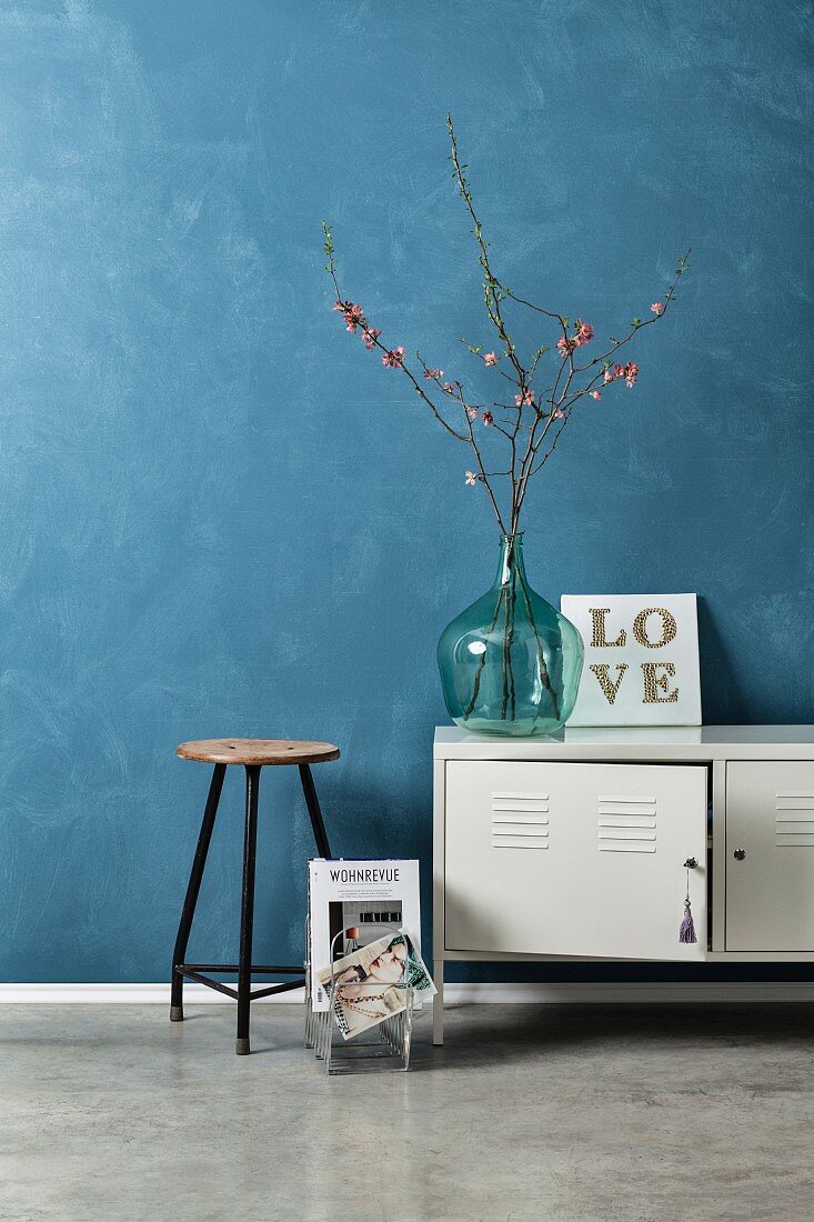 Vintage Setting für ein DIY Typo-Bild: alter Hocker, Metallspind und Blütenzeige in Glasballon vor blau marmorierter Wand