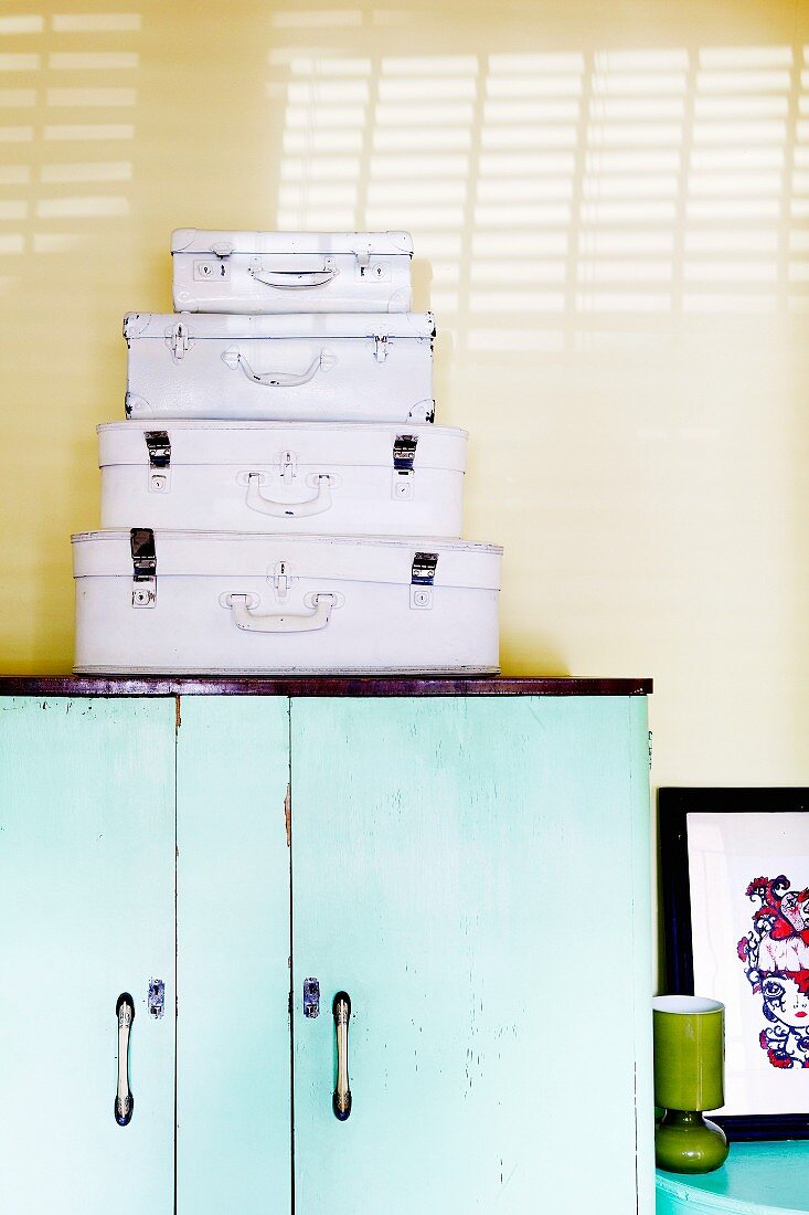 Stacked set of white suitcases on half-height, turquoise cabinet against yellow wall