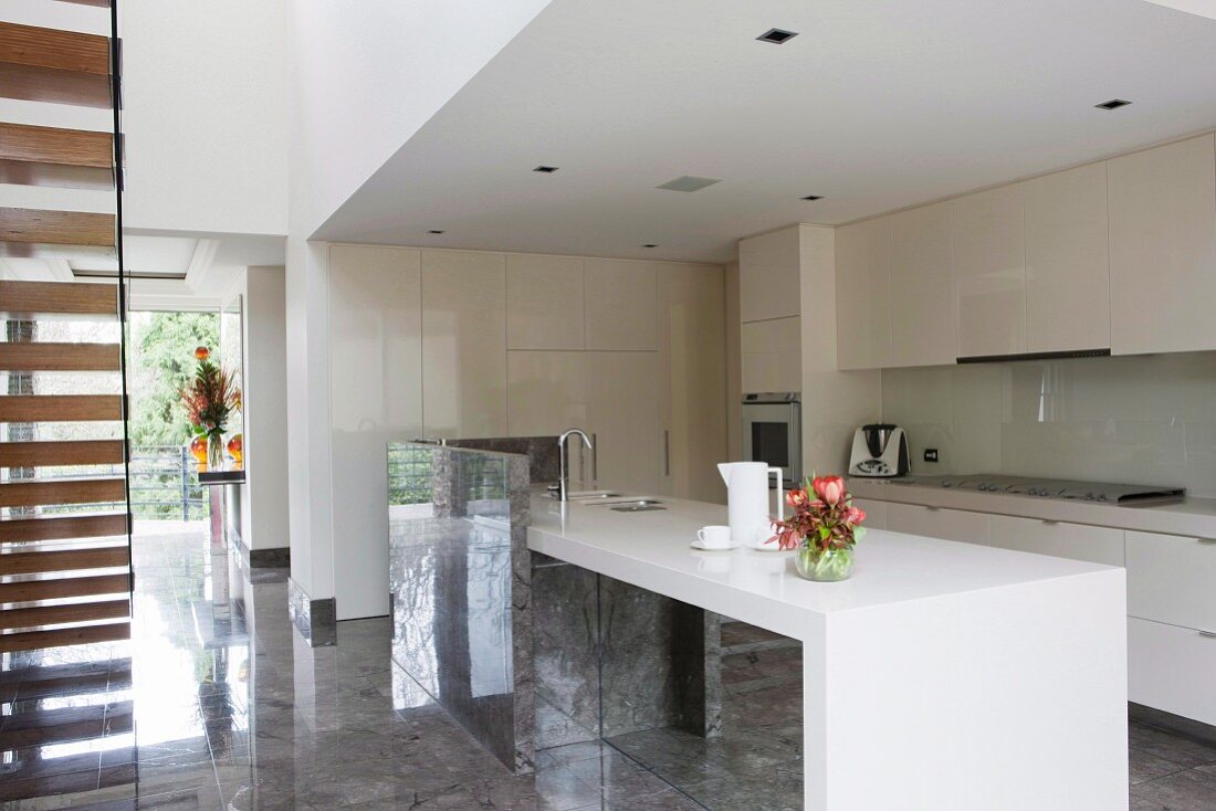 Open-plan, designer fitted kitchen with white counter and glossy stone floor in modern house