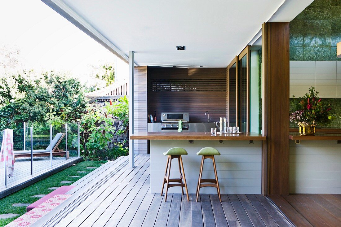 Bar counter and bar stools on veranda of modern house with view into garden