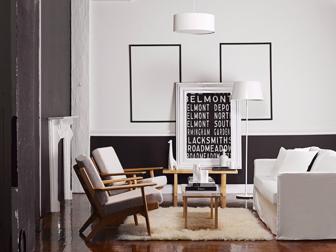 Living room with black-painted dado and modern artwork with lettering motif in front of empty picture frames behind seating group with pale upholstery