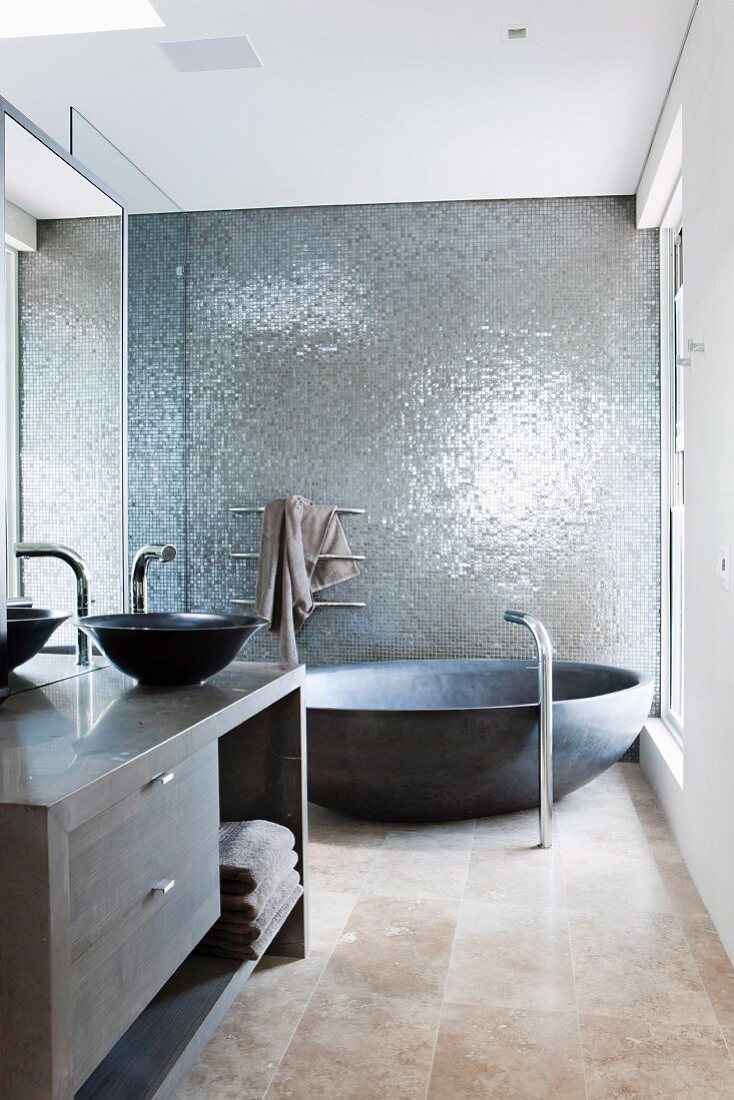 Designerbad mit runder Wanne vor grau schimmernder Wandstruktur und Waschtisch mit anthrazitfarbener Schüssel