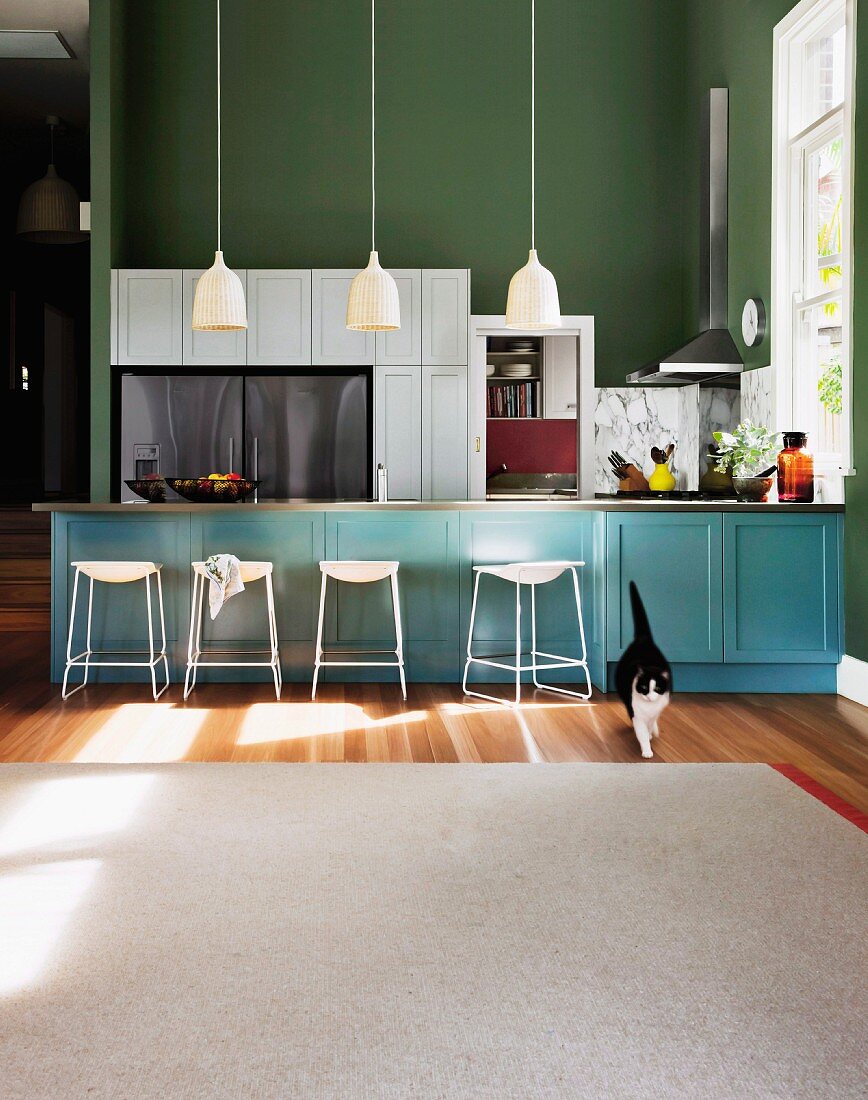 Weisser Teppich vor Theke in Hellblau und Barhocker, darüber Pendelleuchten, in offener Küche mit grün getönter Wand,