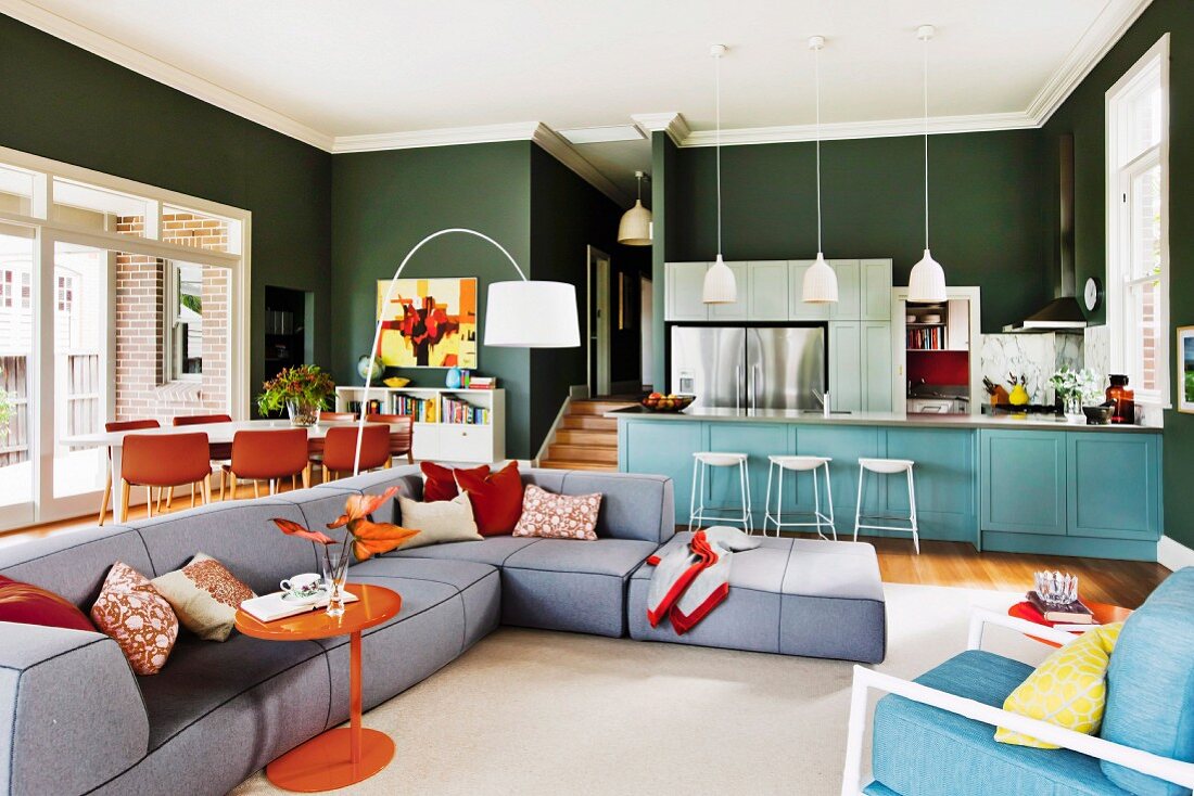 Sofalandschaft, Essbereich und Küchentheke in offenem Wohnraum mit grüner Wand