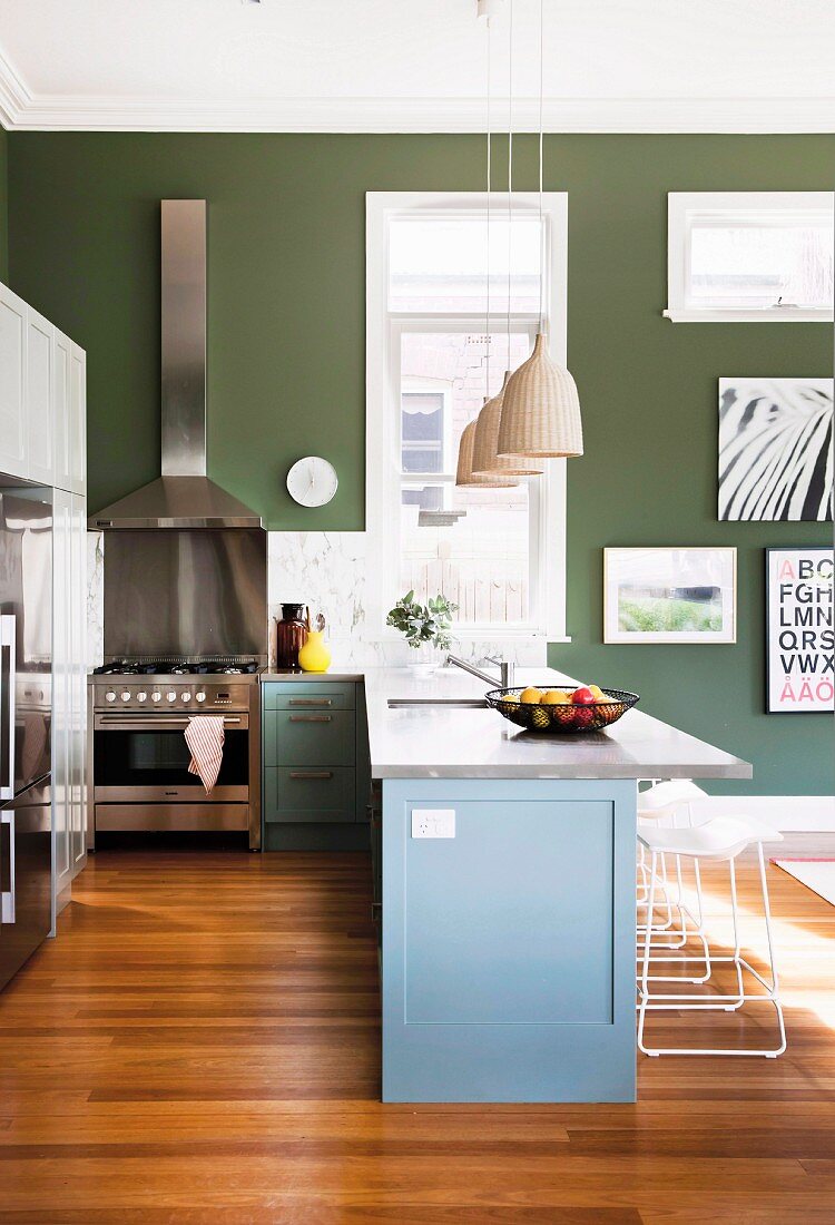Kitchen counter painted grey-blue on wooden floor in warm shade and stainless steel cooker against dark green wall in open-plan interior