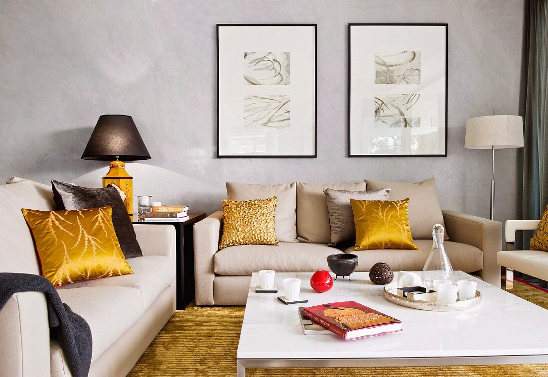 Helle Sofagarnitur und Kissen mit goldgelbem Seidenbezug um modernen Coffeetable in elegantem Wohnzimmer mit grau marmorierten Wänden