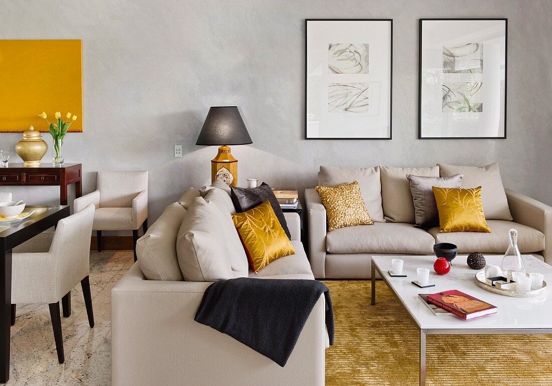 Elegant sofa set with gold scatter cushions and modern coffee table in living room painted pale grey with dining set to one side