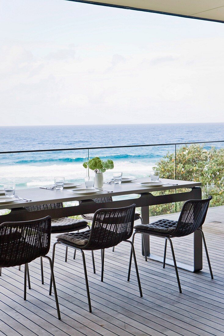 Black mesh chairs around set table on wooden deck with panoramic view of Pacific Ocean