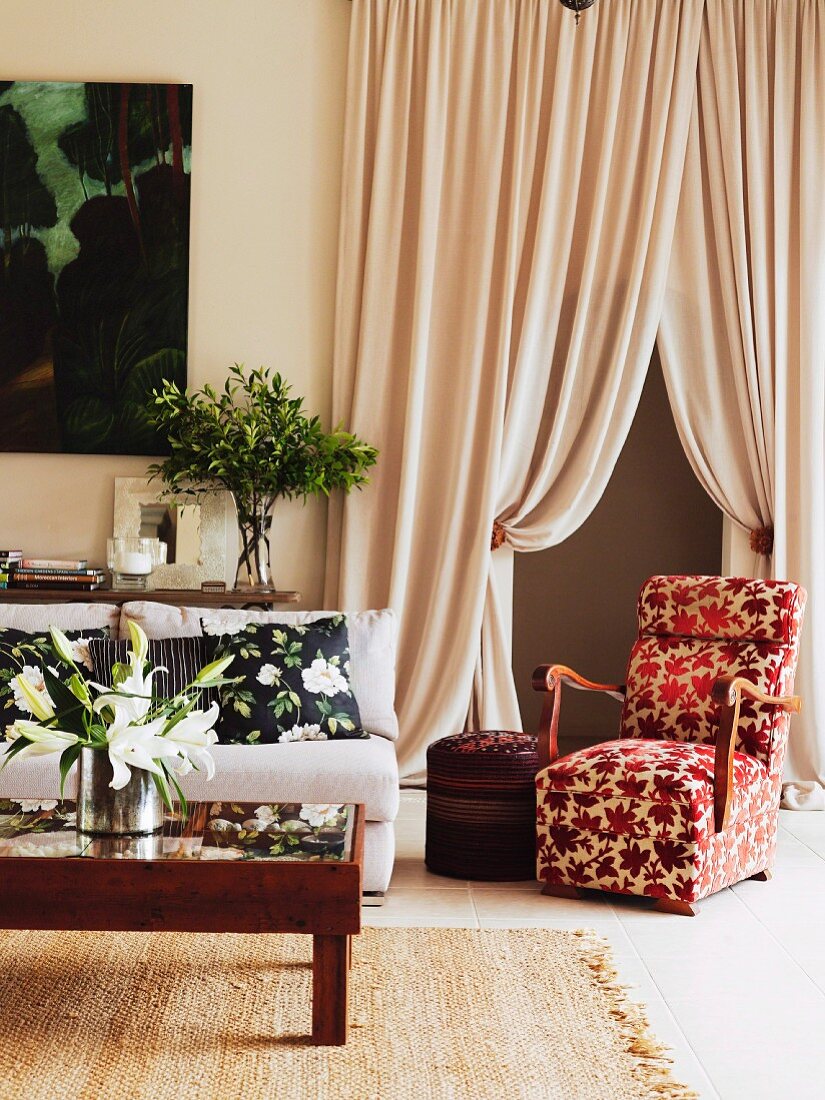 Elegant armchair with red and white floral cover in front of draped, floor-length curtains in traditional interior