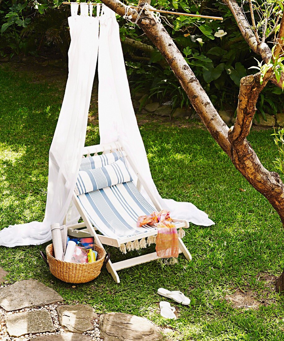 Rustic deckchair with striped seat under white fabric canopy hanging from tree in garden