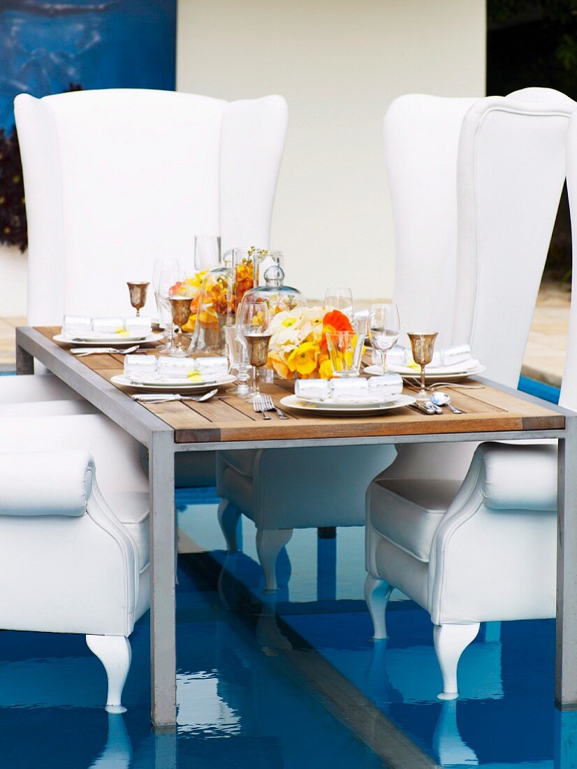 Festively set table and throne-like, white, upholstered armchairs on special floor insert in swimming pool