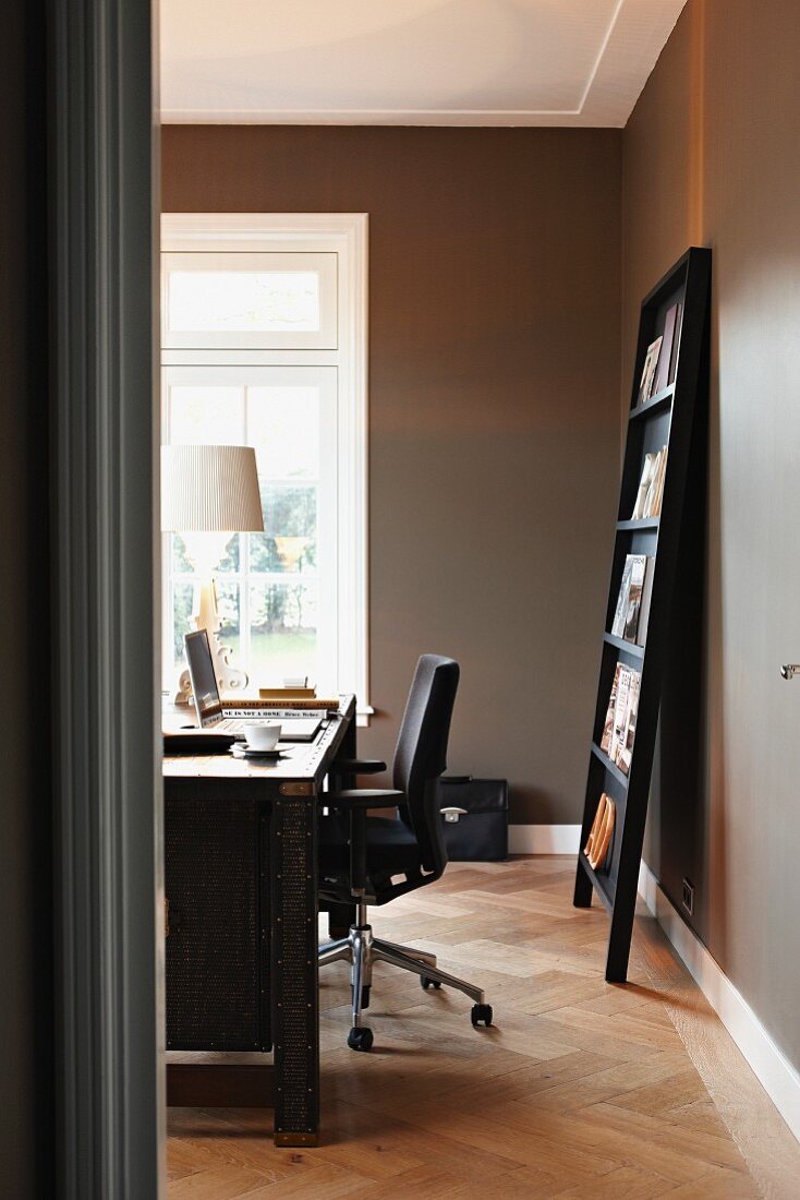Blick auf Schreibtisch und an die Wand gelehnten Zeitschriftenständer in grau getöntem Home-Office
