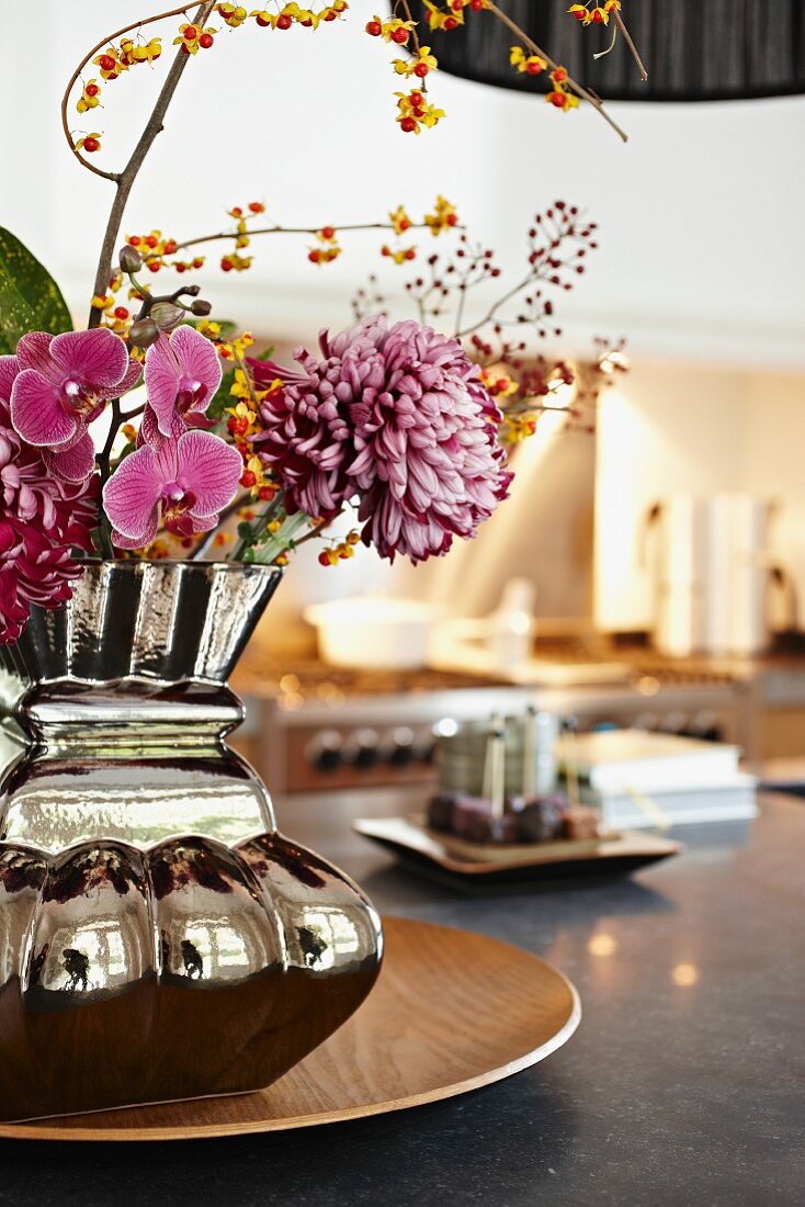 Spiegelnde Vase mit Blumen und Gasherd unscharf im Hintergrund