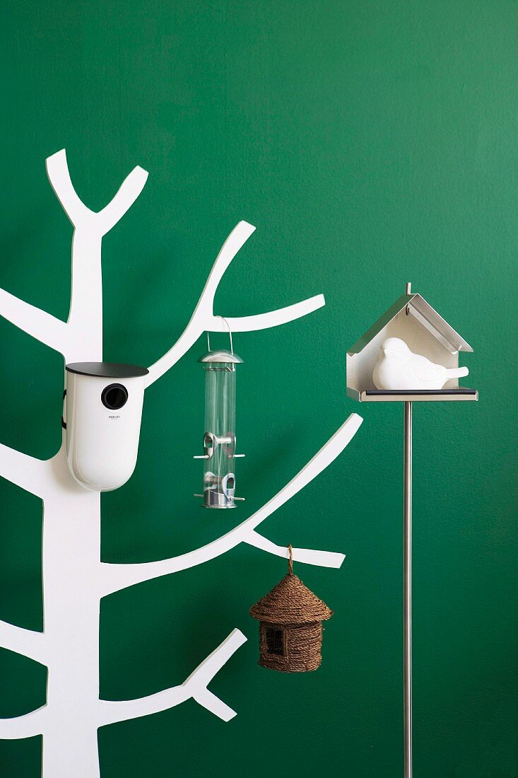 Verschiedene Vogelhäuschen auf weißem, stilisiertem Holzbaum gehängt, vor grüner Wand