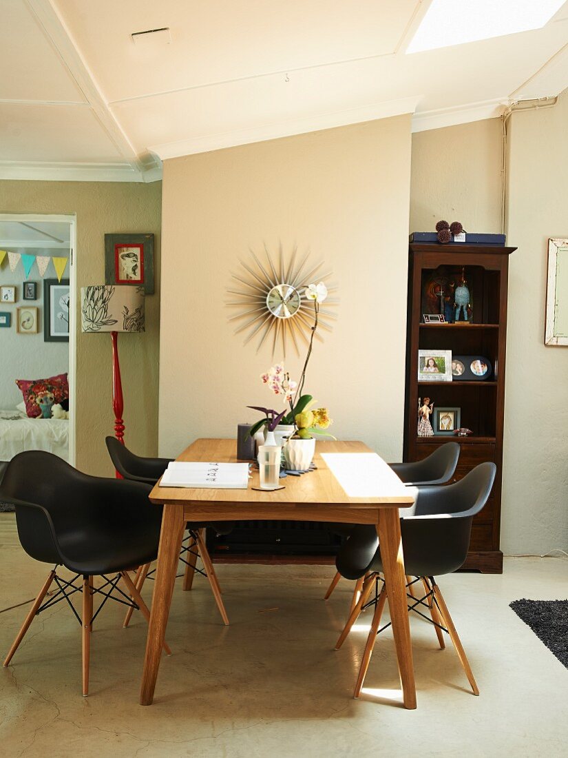 Dining area with black designer chairs around wooden table; sunburst clock on wall