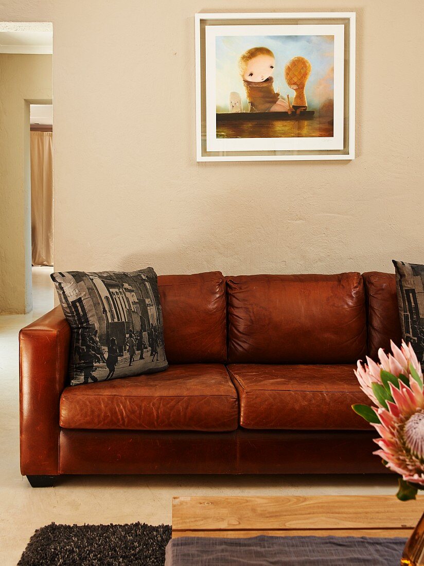 Framed picture above brown leather sofa; arrangement of protea flowers in foreground