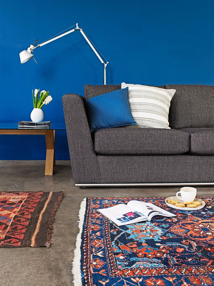 Dunkelgraues Sofa, Designer-Stehleuchte und gemusterte Orientteppiche vor intensiv blau getönter Wand