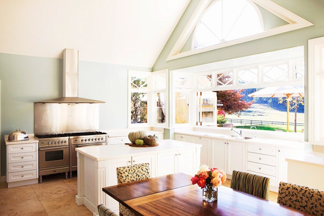 Glazed gable and folding glass door in spacious kitchen with island counter and twin stainless steel, gas cookers