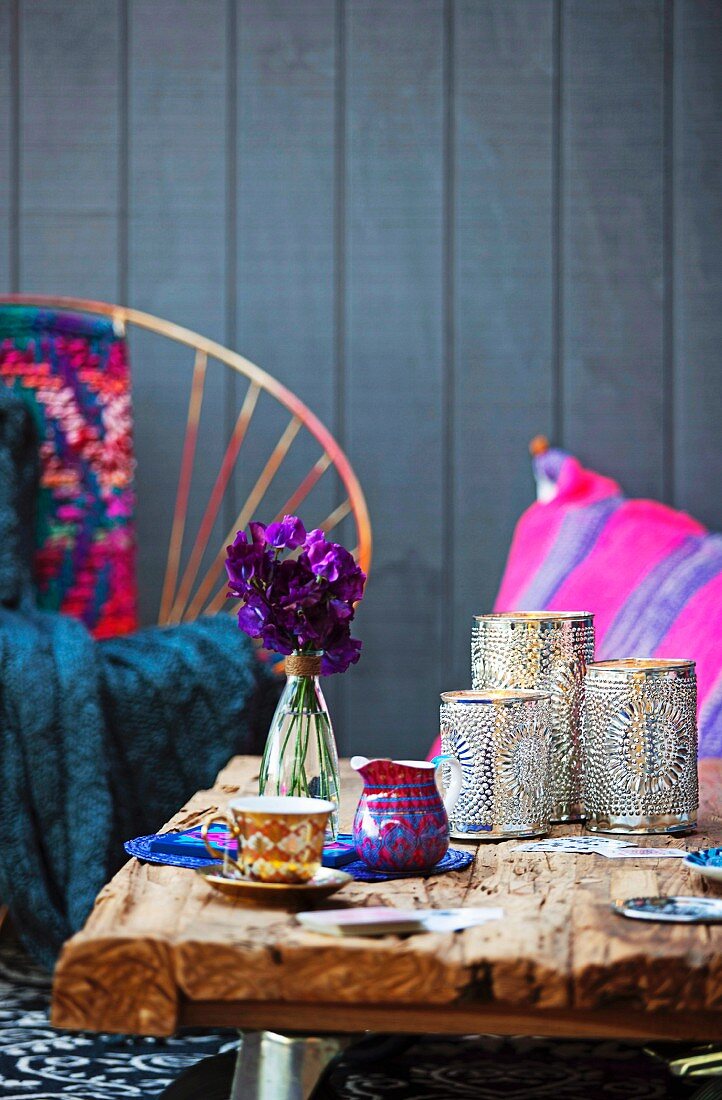 Marokkanische, silberne Windlichter und Mokkatasse auf rustikalem Holztisch; bunte Kissen und Holzverschalung im Hintergrund