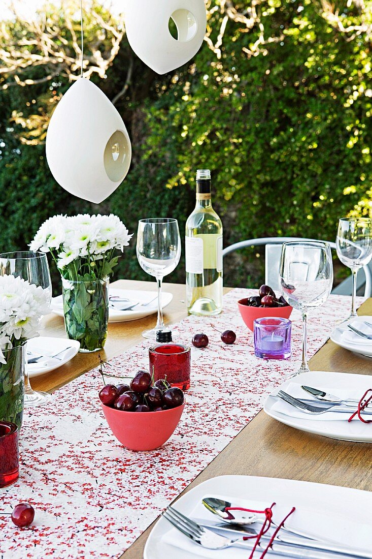 Gedeckter Gartentisch mit Obstschalen unter weissen Lampions