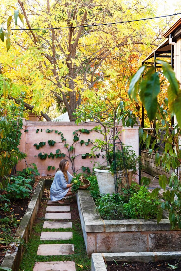 Woman next to raised bed with stone wall in autumnal garden