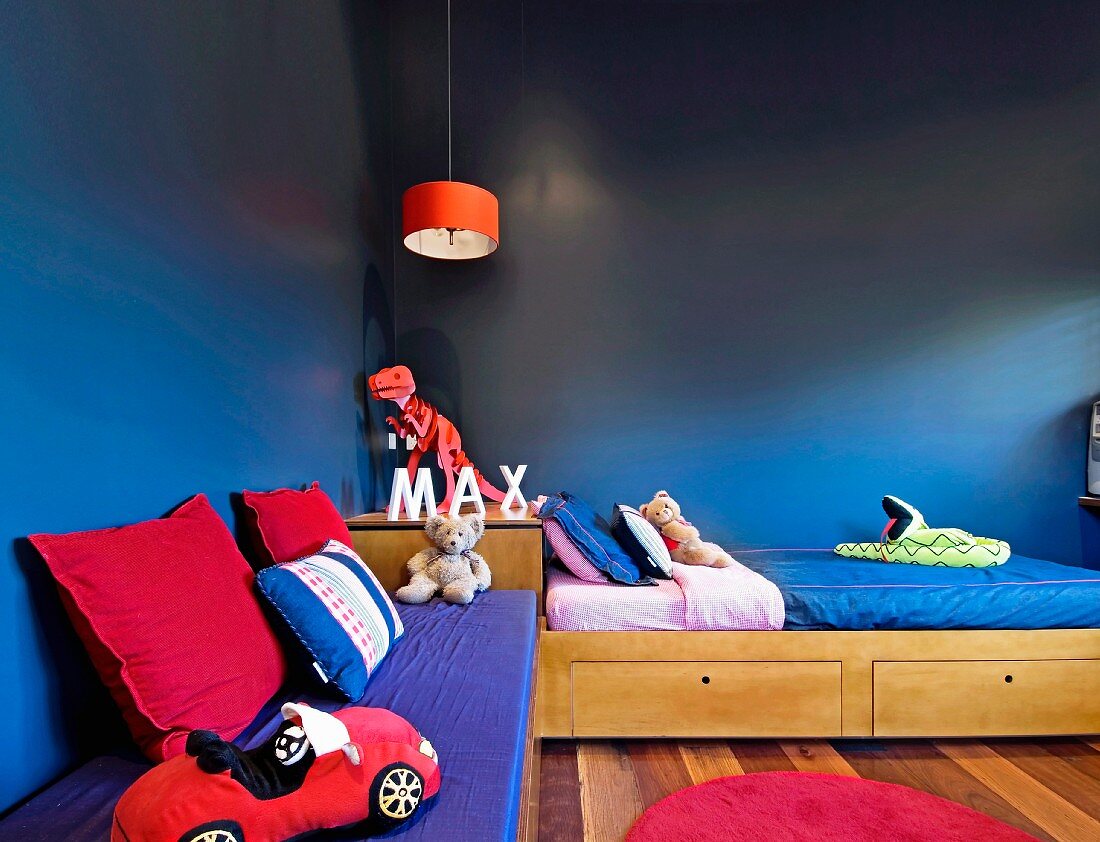 Child's bed and bench with cushions and toys in corner of bedroom painted deep blue