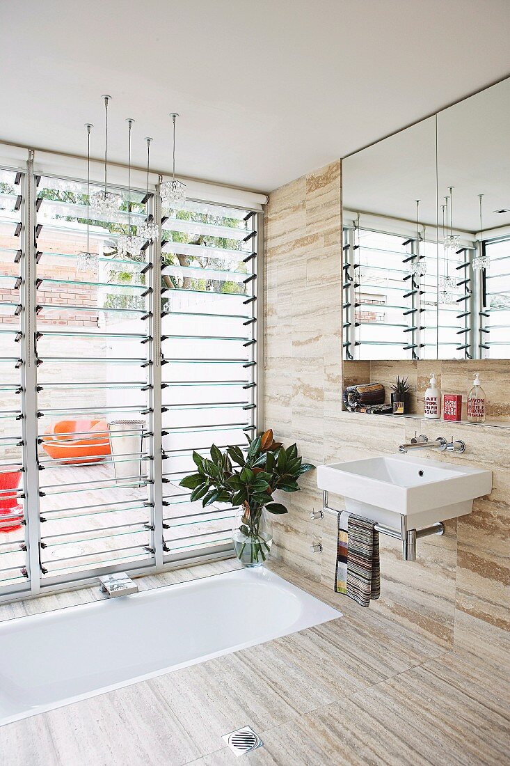 Designerbad mit in Boden eingelassener Badewanne, vor halboffenen Glaslamellenfenstern und Blick auf Terrasse