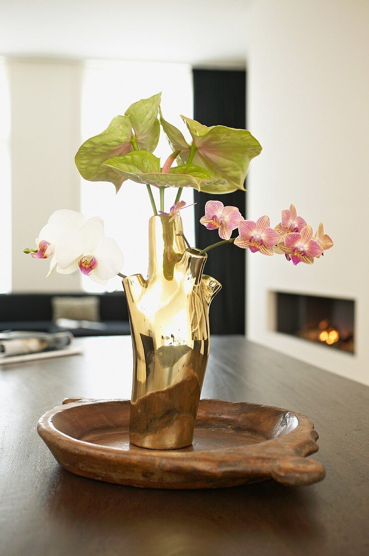 Goldfarbene Designer-Vase mit Orchideen und Anthurie auf Esstisch