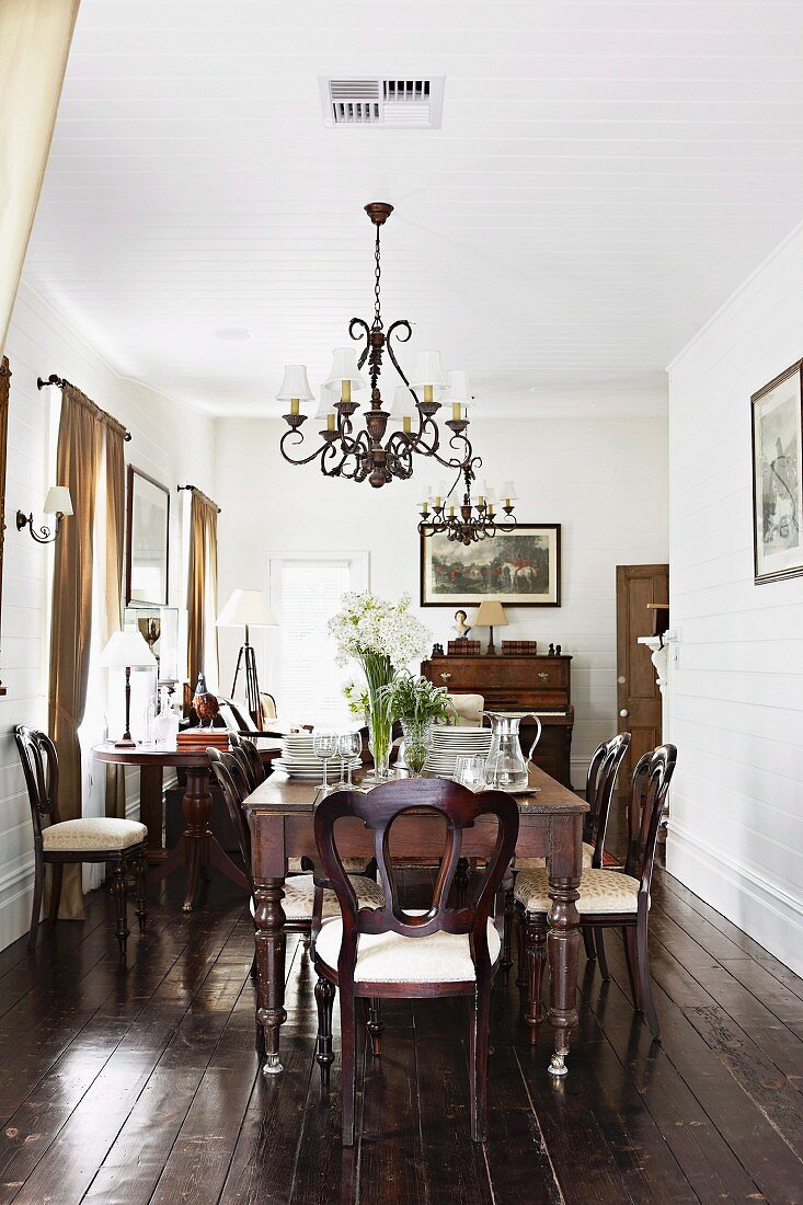 Dining table, antique chairs, wrought iron chandelier and dark wooden floor in traditional, elegant dining room