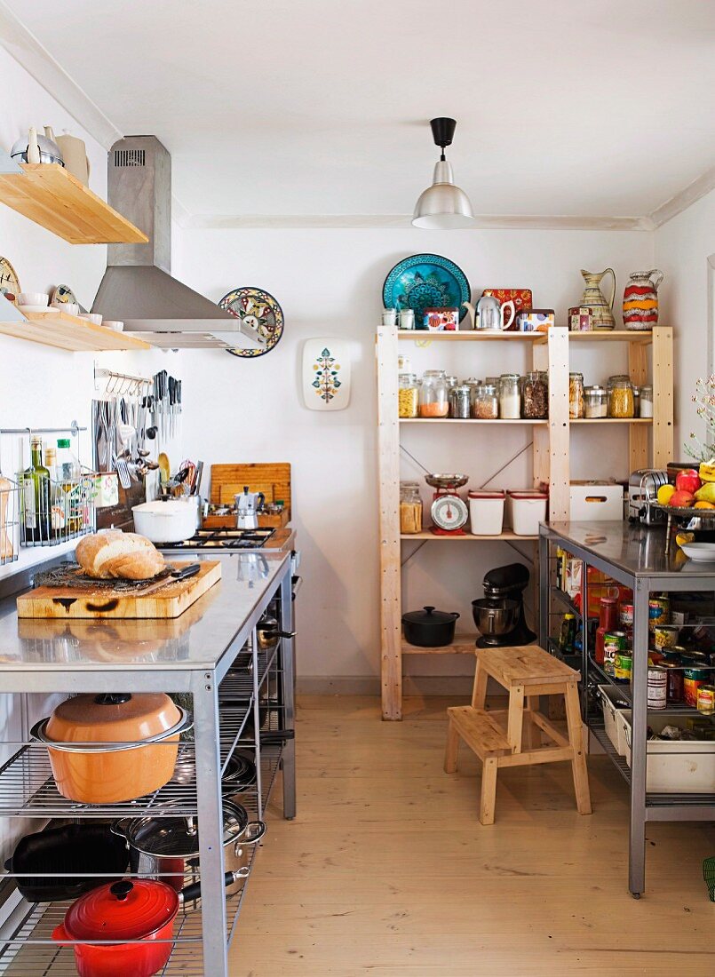 Counters with open-fronted shelves below and tall wooden shelves in kitchen