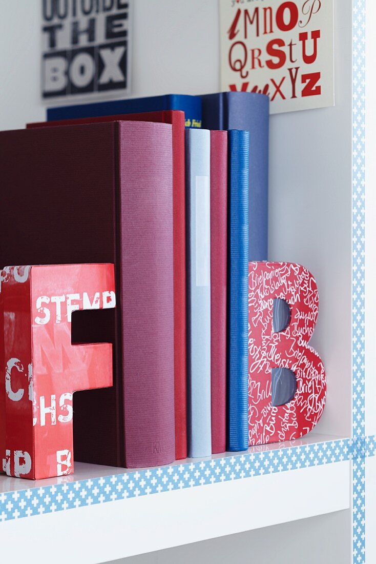 Farbige Buchstaben-Schachteln als Buchstützen in weißem Bücherregal
