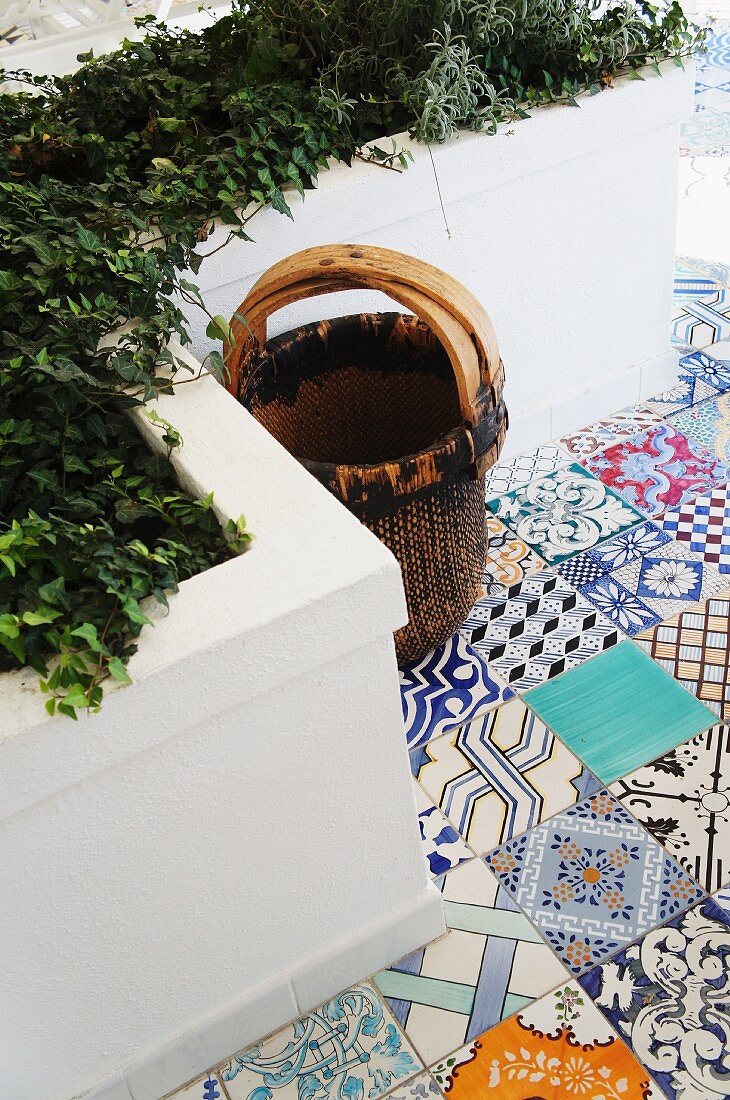 Basket on Mediterranean terrace with colourful, patterned floor tiles and masonry raised beds