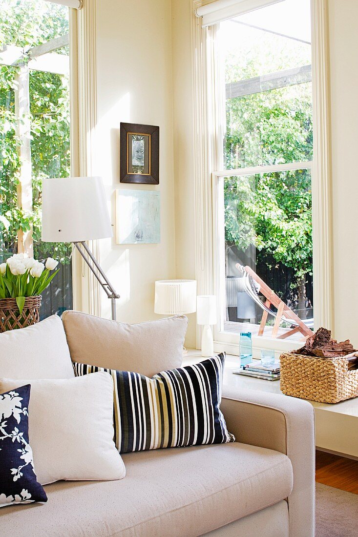 Fensterecke im sonnigen Wohnraum mit Dekokissen auf hellem, zeitlosem Sofa