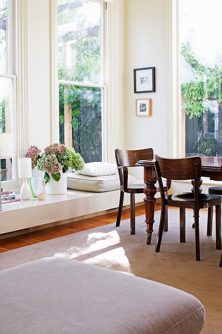 Antique table in corner of sunny dining area with multiple windows and low, broad windowsill