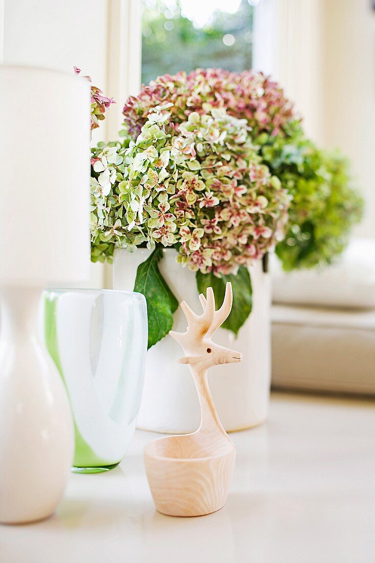 Fensterbank-Deko mit Vasen, Hortensienblüten und einem Schälchen mit Griff in Form eines stilisierten Elchkopfs