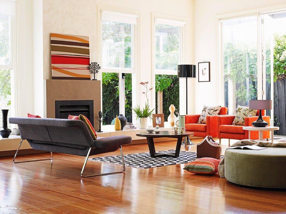 Seating in various colours, coffee table and open fireplace in corner of high-ceilinged, bright interior