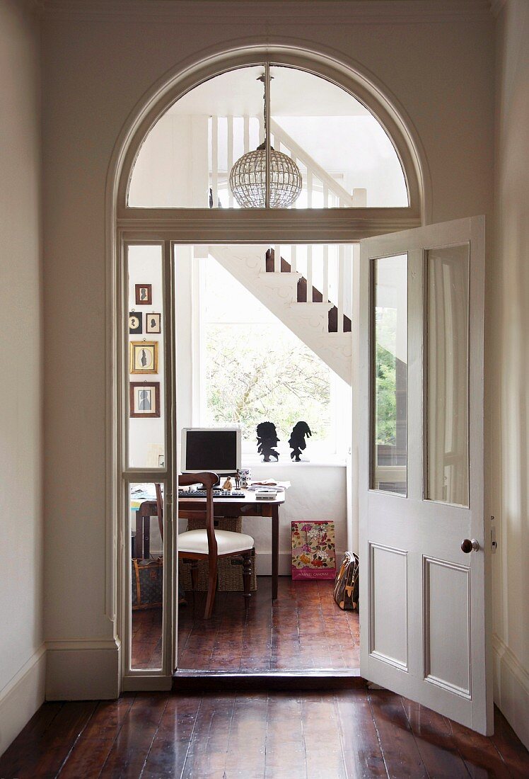 Foyer in grand house with view through arched doorway into stairwell with desk below window